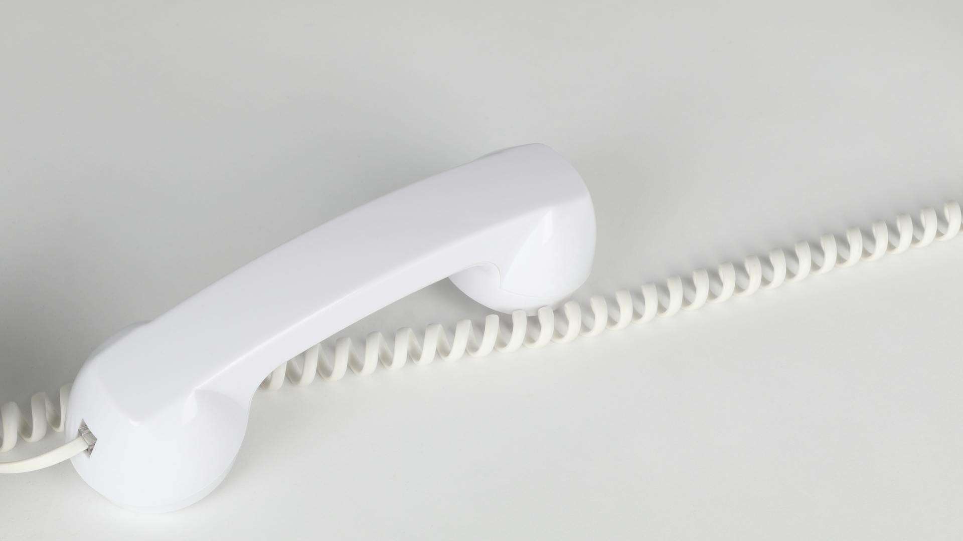 White corded telephone handset on a clean white surface, representing automated phone answering AI